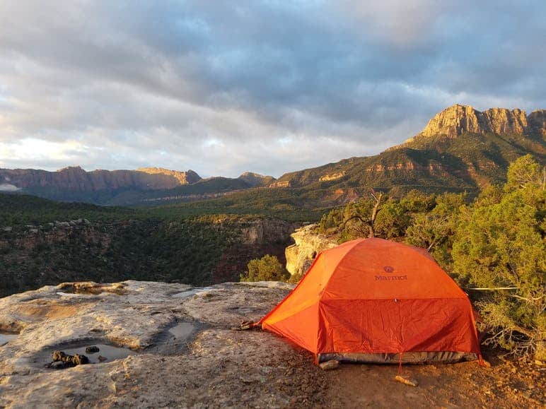 An orange dome tent perched on a rock cliff overlooking Zion National Park in Smithsonian Butte Dispersed Camping Area.