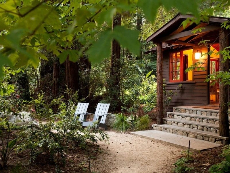 A wood cabin in a forested section of Big Sur with Adirondack chairs in front - part of a California National Park road trip itinerary.