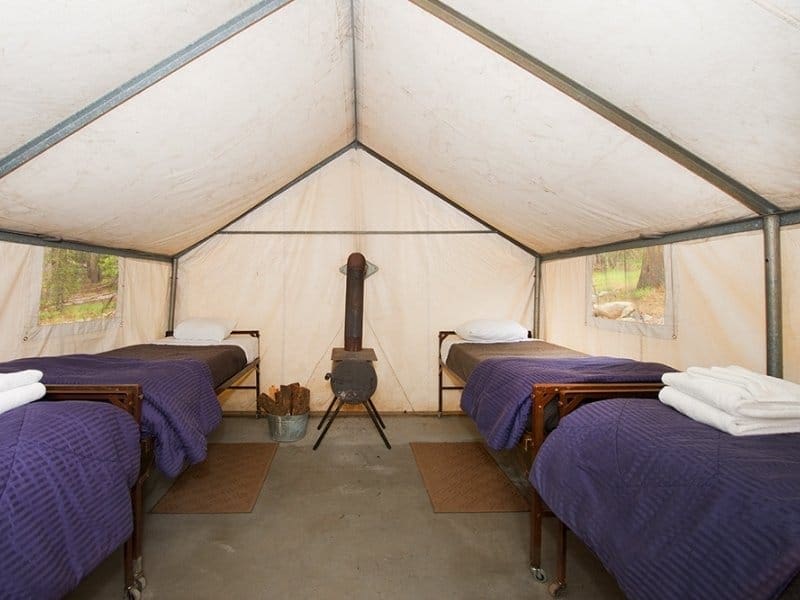Interior of a canvas tent cabin at Tuolumne Meadows Lodge in Yosemite with four single beds and an inside wood-burning fireplace.