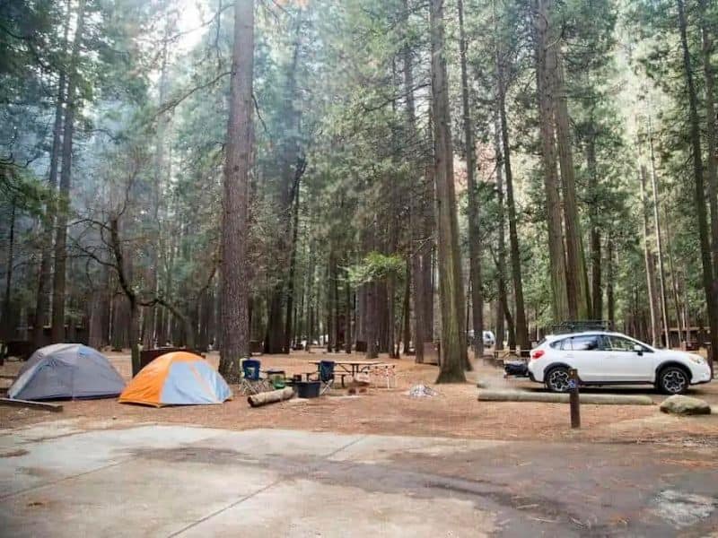 A shaded campsite at Upper Pines Campground in Yosemite National Park with two pitched tents, a picnic table, and a white Subaru vehicle.