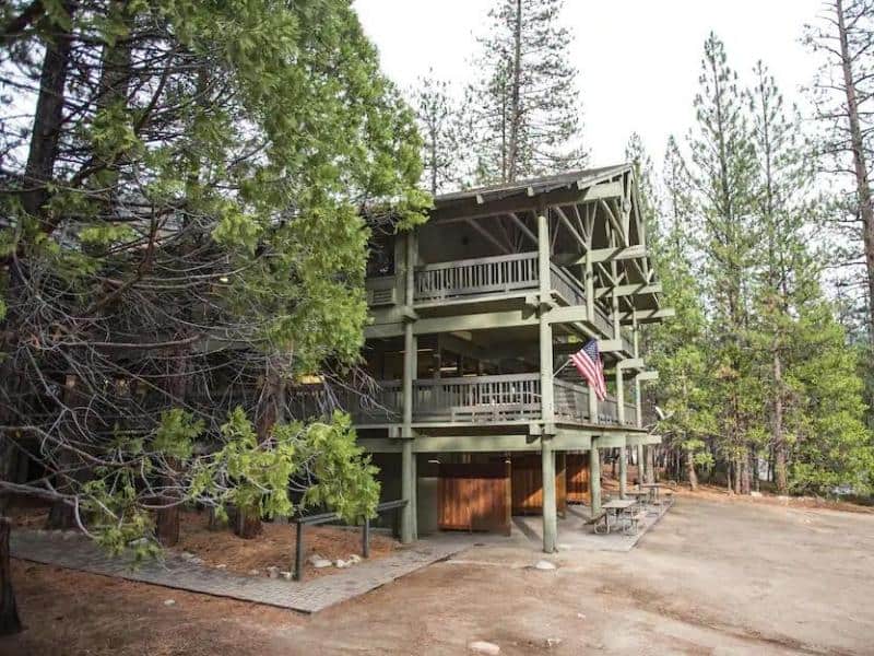 Multi-story Cedar Grove Lodge with green exterior, wooden balconies, and American flag, tucked in the forest of Sequoia National Park.