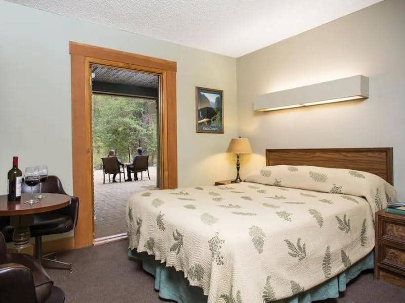 Guest room at Cedar Grove Lodge with a queen bed, green fern-patterned bedspread, and a view onto the balcony. A lesser known area to stay in Sequoia National Park.