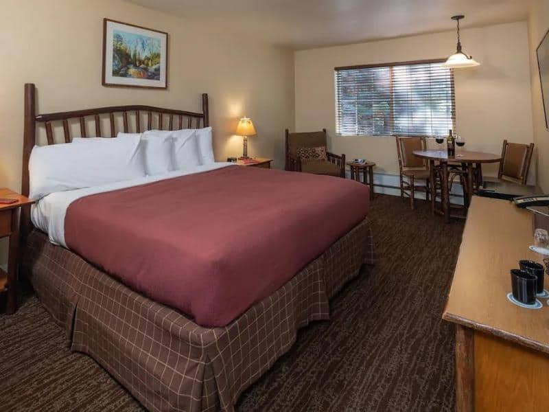 Standard room at John Muir Lodge featuring a king-sized bed with a maroon bedspread, artwork above the headboard, and a dining area. One of the most popular places to stay in Sequoia.