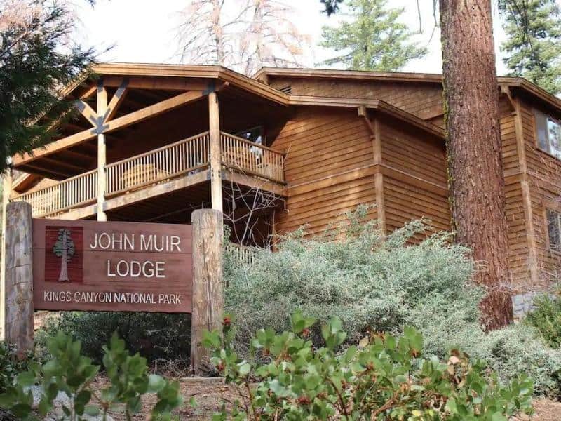 Exterior view of John Muir Lodge with a wooden sign at the entrance, surrounded by trees in Kings Canyon National Park, adjacent to Sequoia National Park.