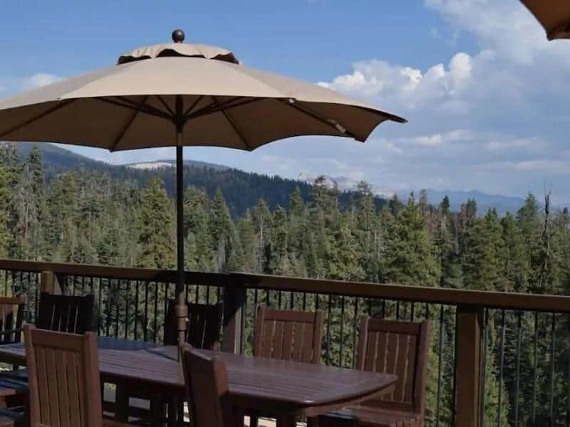 Outdoor dining area on a wooden deck at Montecito Sequoia Lodge with panoramic views of the forest. Year-round family-friendly lodging near Sequoia.