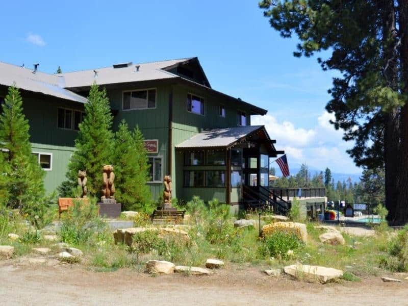 Montecito Sequoia Lodge exterior with green siding and a welcoming porch, flagged by wooden bear sculptures - a family-friendly lodging option near Sequoia National Park.