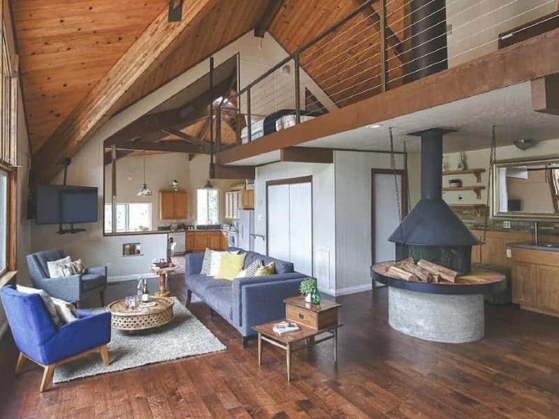 Spacious living area with high ceilings, modern furnishings, and a central fireplace at a Sequoia vacation rental located inside the park gates.