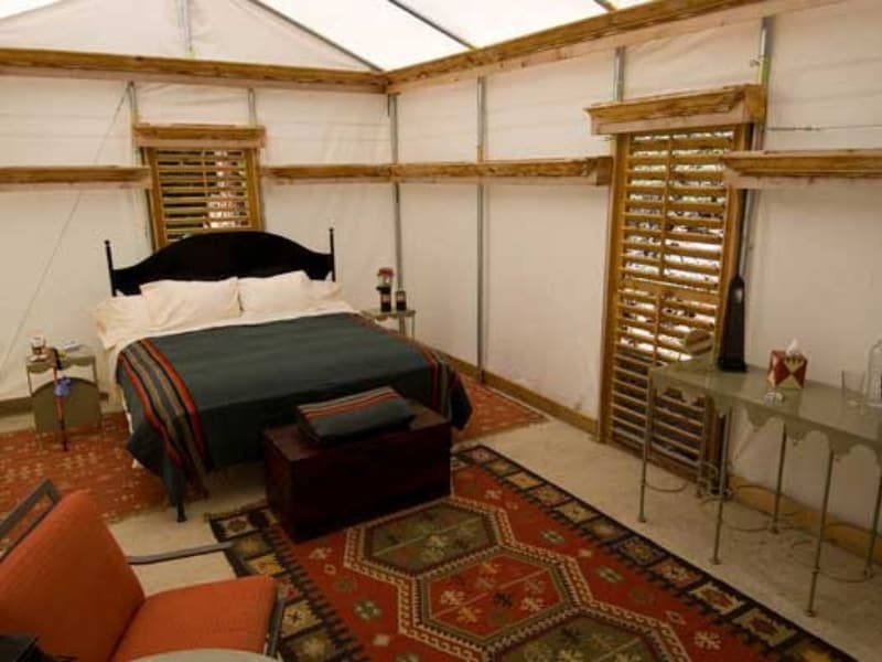Interior view of a spacious canvas tent with a large bed, patterned rugs, and a vanity set at Sequoia High Sierra Camp, a glamping site in Sequoia National Park, CA.