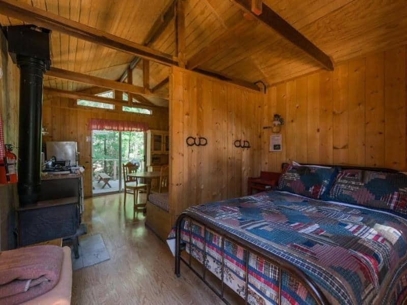 Cozy cabin interior at Silver City Mountain Resort featuring a wood stove, a bed with patchwork quilt, and a view to the porch. Part of a guide on where to stay in Sequoia National Park.