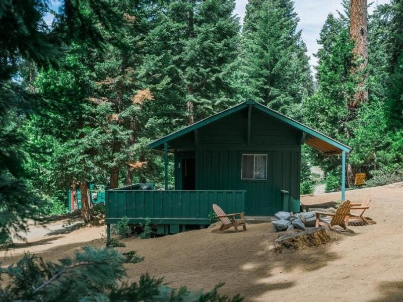 Green cabin at Silver City Mountain Resort with a front porch and Adirondack chairs, set in a pine forest in the Mineral King region of Sequoia National Park.