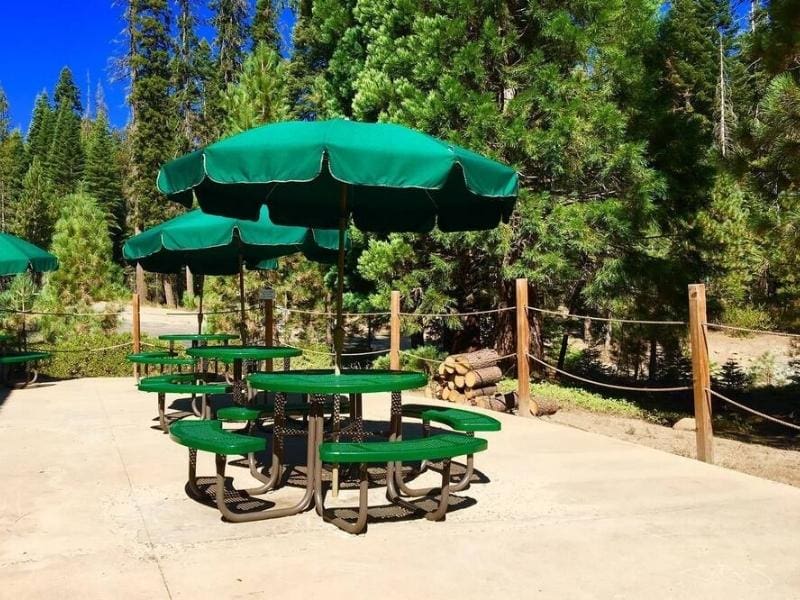 Round outdoor table with an attached green umbrella for shade at Stony Creek Lodge near Sequoia National Park.