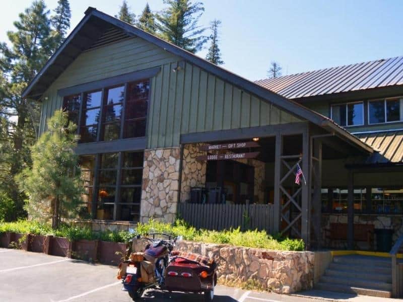 Stony Creek Lodge's main entrance with large windows and stone accents, and a motorcycle parked out front. Based lodge-style accommodation near Sequoia National Park.