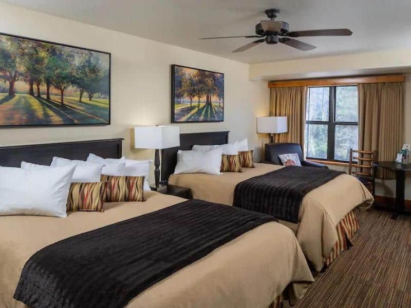 A Wuksachi Lodge guest room with two queen beds, black comforters, and framed artwork of a tree-lined road; Sequoia National Park's premier luxury lodge.