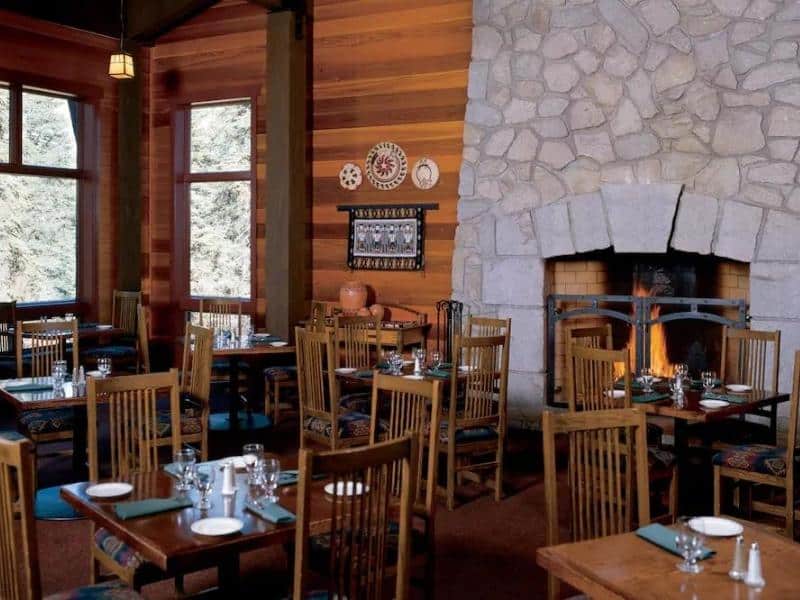 Cozy dining area inside Wuksachi Lodge in Sequoia National Park featuring wooden tables, chairs, and a large stone fireplace.