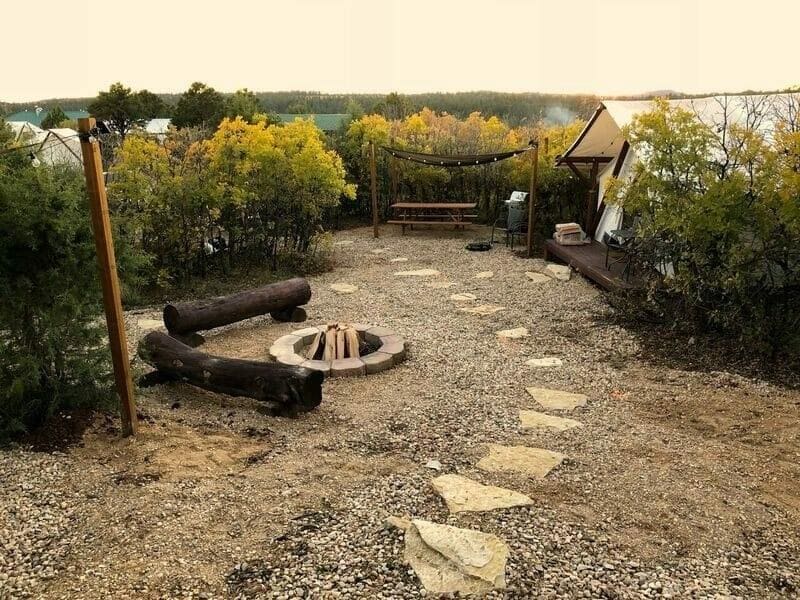 Outside view of glamping site at Zion Ponderosa Ranch near Zion NP with fire pit, log seating, and path leading to glamping tent and picnic table