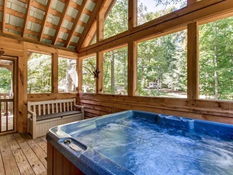 Indoor hot tub room enclosed in a wood-paneled space with large windows offering views of the surrounding woods.