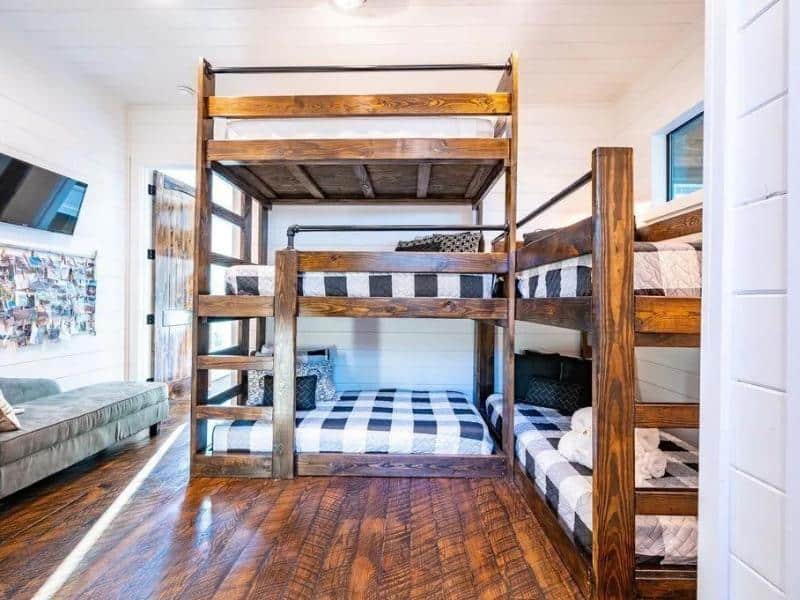Bunk room with sturdy wooden beds and plaid bedding, alongside a mounted television in a Broken Bow Vrbo rental.
