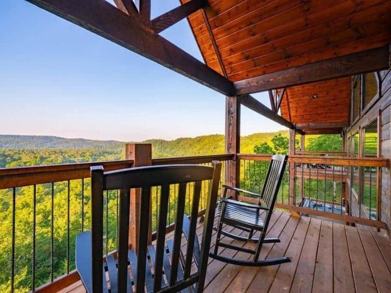 Scenic balcony view from 'High Faultin' Hideaway', with rocking chairs overlooking greenery and distant hills, a serene. Part of a guide to the best luxury cabins in Broken Bow.