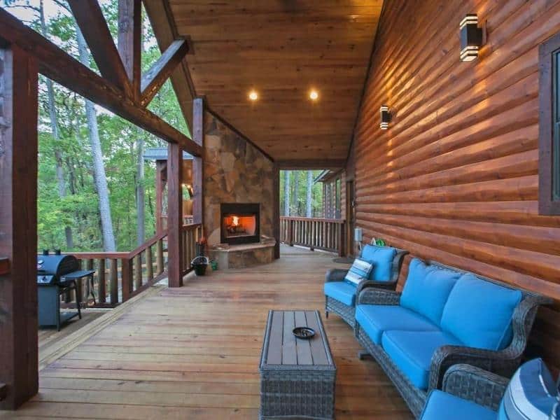 Outdoor covered deck with a stone fireplace and plush seating.