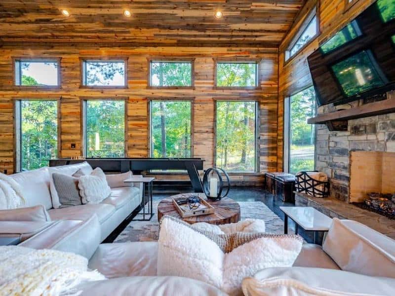 The living area inside 'Somethin 2 Talk About', a Broken Bow Vrbo rental with a rustic design with large windows, wooden walls, and comfortable cream sofas.