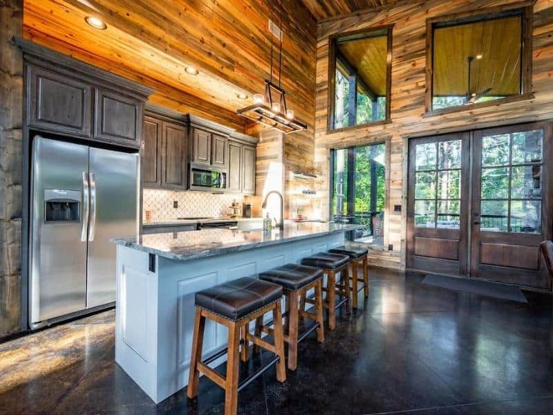Kitchen space featuring dark cabinetry, a long island with bar stools, and stainless-steel appliances in a luxury cabin in Broken Bow.
