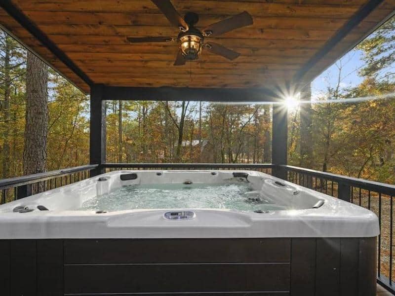 Outdoor hot tub on a deck surrounded by towering trees with sunlight filtering through in Broken Bow, OK.