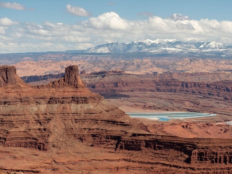 Scenic vista over Dead Horse Point State Park with layered red rock canyons and snow capped mountains in the distance.