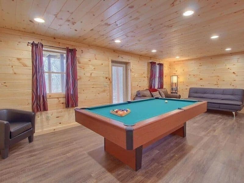 Recreational area inside a cabin with a pool table, wooden walls, and comfortable seating in a Hocking Hills Vrbo cabin.