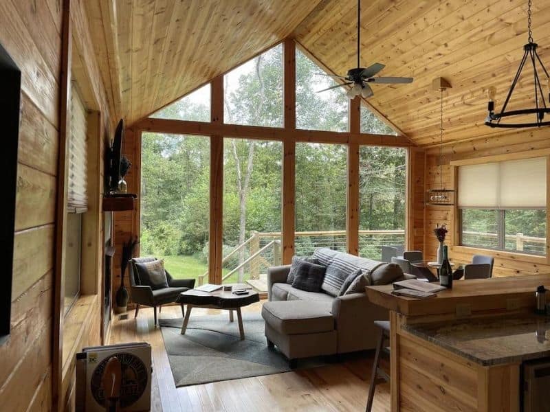 Spacious living area in a Hocking Hills cabin with vaulted ceilings, large windows overlooking the forest, and comfortable gray sectional sofa.