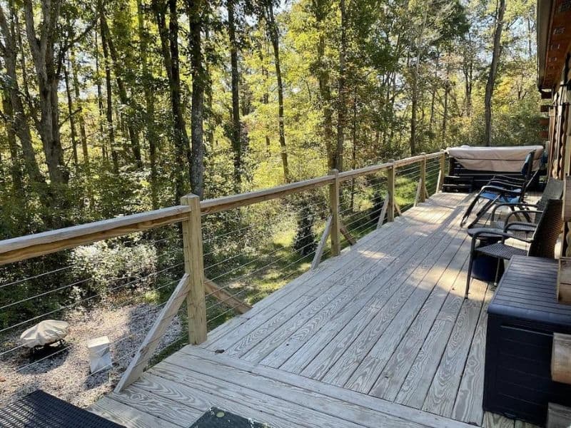 Sunlit deck of a luxury cabin in the Hocking Hills OH area surrounded by greenery, furnished with outdoor lounge chairs.