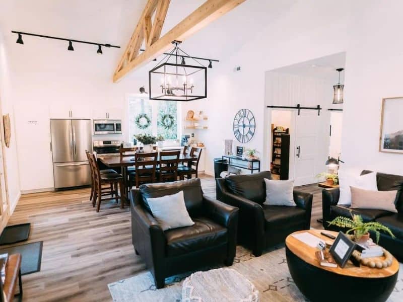 Luxurious open-concept living space in a Hocking Hills cabin, with stylish black leather couches, a modern kitchen, and exposed wooden beams.