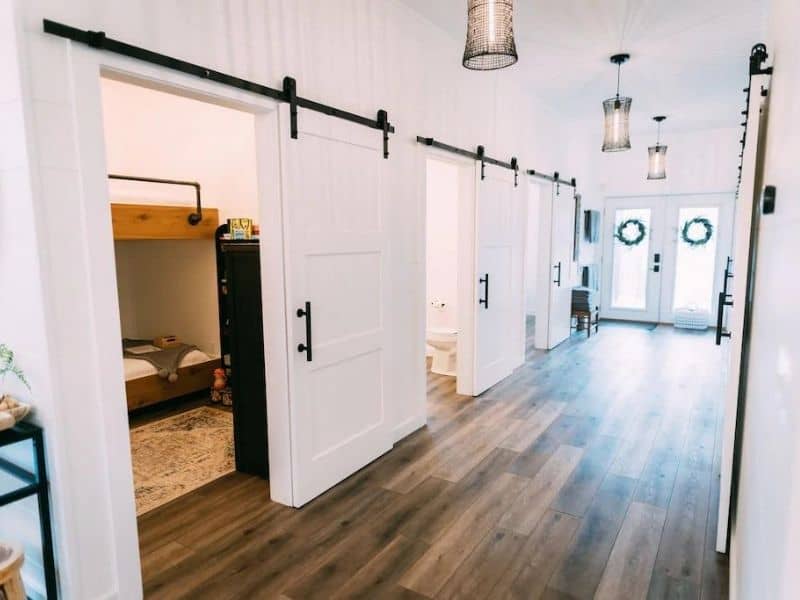 Modern cabin hallway with white sliding barn doors, stylish hanging lights, and a peek into the inviting bedrooms of a Hocking Hills luxury cabin rental on Vrbo.