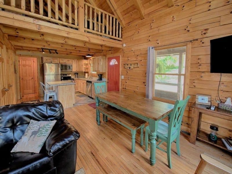 Open-concept living and dining area with a lofted ceiling, a wooden dining table, and a kitchen with modern appliances at Liberty Ridge Pet-Friendly Cabin in Hocking Hills.