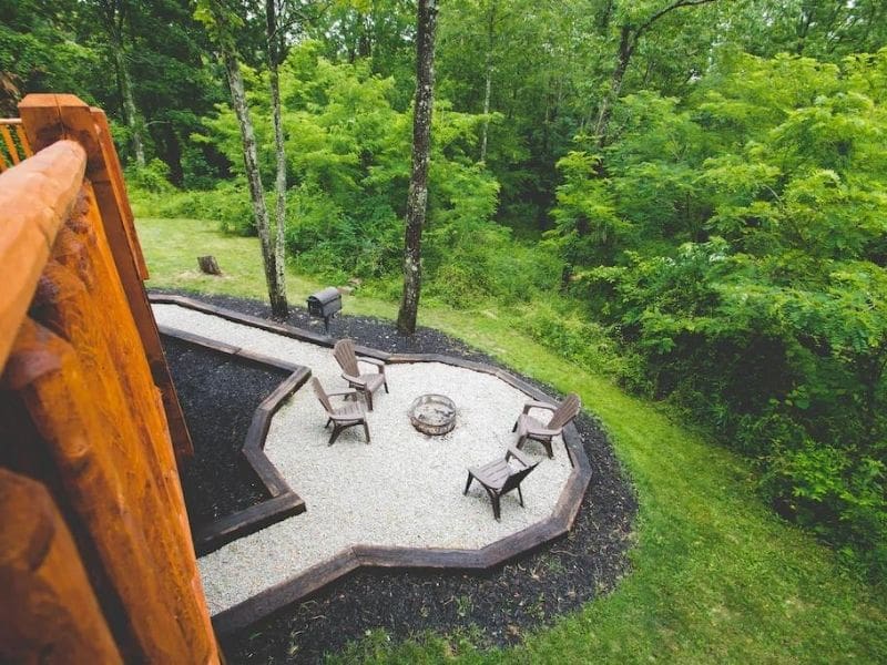 Outdoor fire pit area surrounded by forest, with comfortable seating.