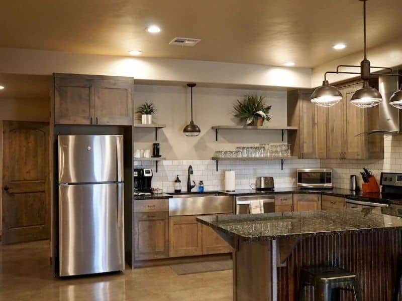 Modern kitchen with stainless steel appliances, floating shelves, and an island counter in a three-bedroom vacation rental in Moab, UT.