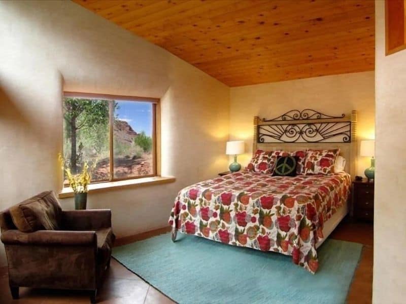 Cozy bedroom at a Moab Vrbo with a wrought iron bed frame, floral bedding, and a window view of the desert landscape.