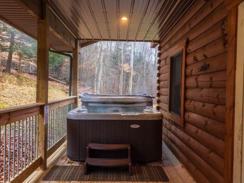 The Peak Pet-Friendly Cabin @ Pine Creek in Hocking Hills, OH. A covered deck with a private hot tub in the corner. The deck is surrounded by wooded scenery.