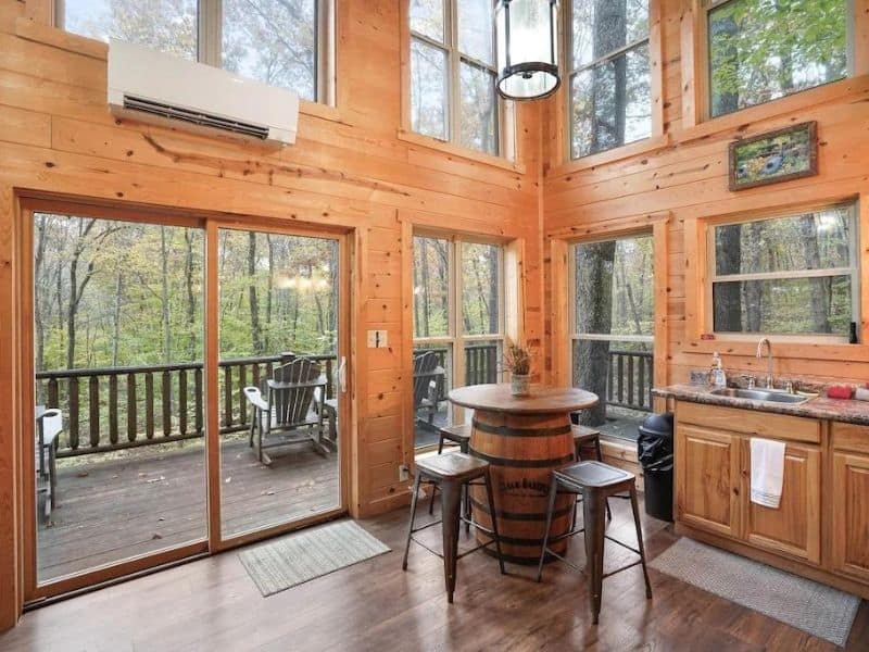 Bright room with large windows and natural wood accents, featuring a barrel table opening onto a deck at a Hocking Hills cabin rental.