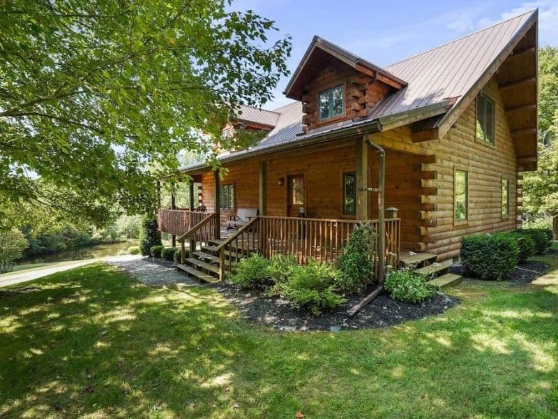 Exterior of a classic log cabin surrounded by greenery, featuring a welcoming porch.