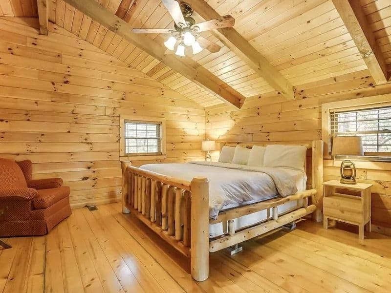 Cozy bedroom with a log bed frame and warm lighting in Whitetail Pines, a luxury cabin retreat in Hocking Hills.