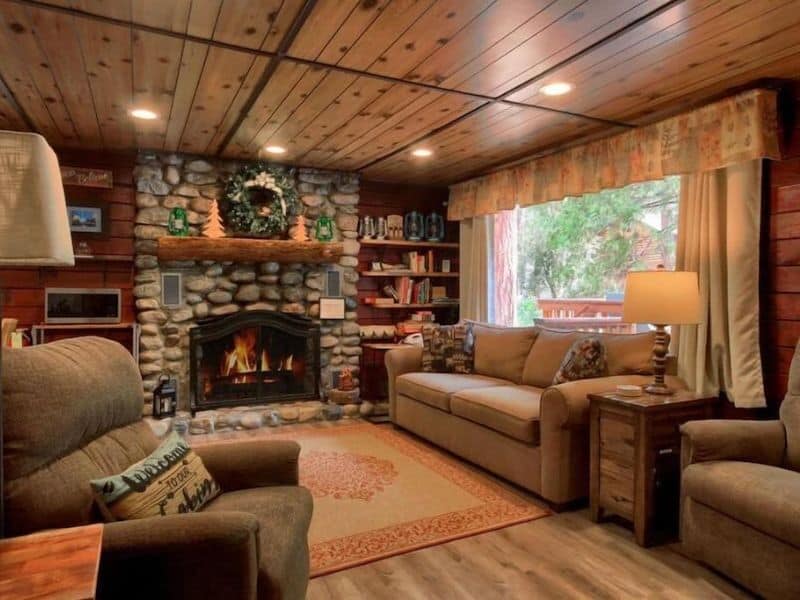Cozy living room inside a Yosemite National Park cabin rental in Wawona with a stone fireplace, plush seating, and a wooden interior.