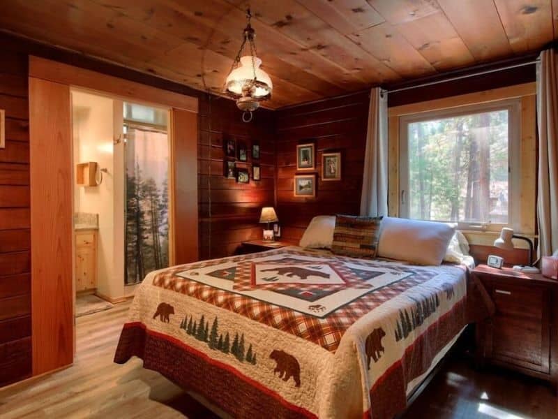 Bedroom in a Yosemite cabin rental with a bear and pine tree-themed quilt and views of the forest through the window.