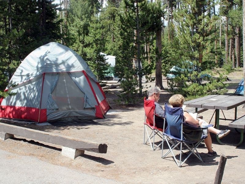 A tent campsite at Grant Village Campground in Yellowstone National Park with two campers sitting in camping chairs