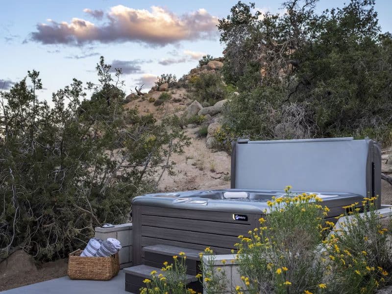 An outdoor hot tub nestled in a desert setting near Joshua Tree. Surrounded by rocks and native vegetation, the hot tub area has beautiful views.
