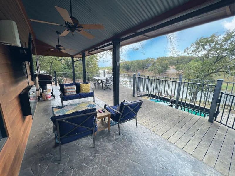 Covered deck at EdgeWater Escape cabin near Turner Falls with outdoor seating, a ceiling fan, a grill, and a view of the lake.