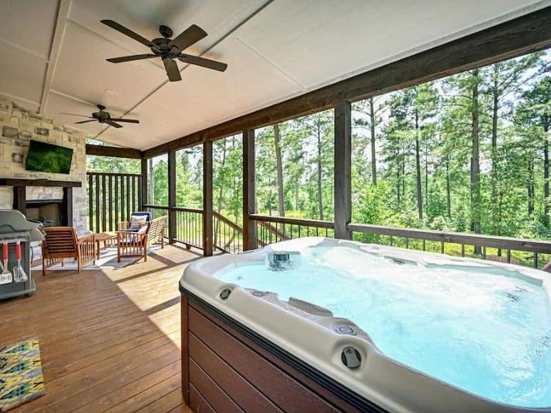 Spacious screened porch with a bubbling hot tub overlooking a serene wooded area in Broken Bow, Oklahoma.
