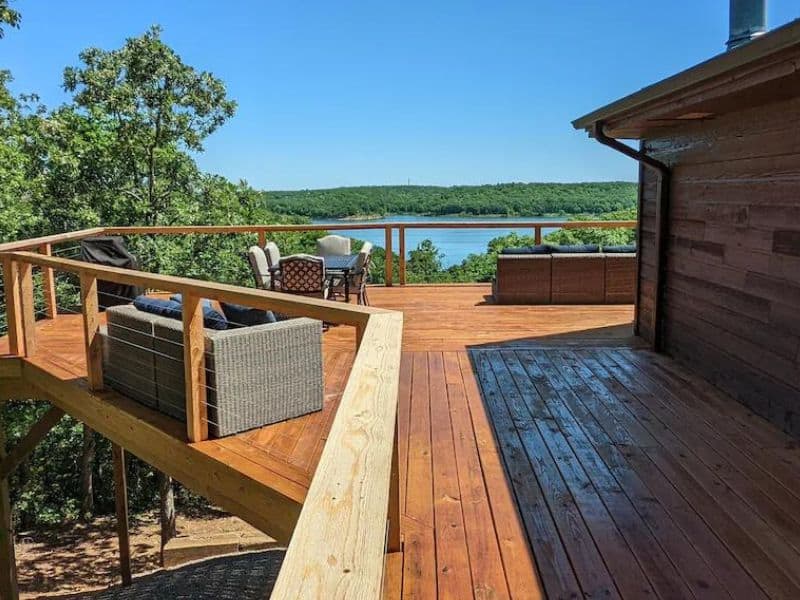 Wooden deck of Lakeview Hideaway, a rental cabin on Lake of the Arbuckles, featuring outdoor seating areas and a scenic view of the lake and surrounding trees.