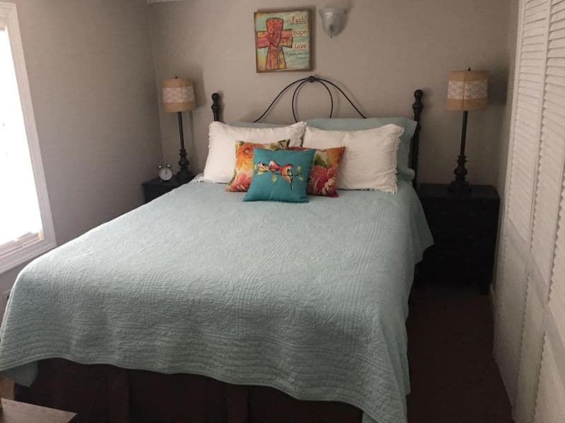 Bedroom in a tiny house rental cabin near Turner Falls with a queen-sized bed, decorative pillows, and bedside lamps.