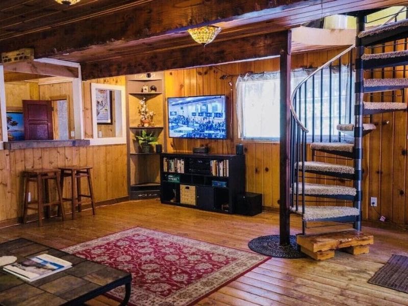 Cabin living room featuring a spiral staircase, a large flat-screen TV, and cozy seating areas. Dog-friendly cabin rental near Yosemite.