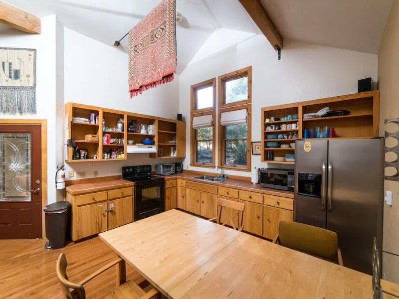 Spacious kitchen with open wooden shelving, a high ceiling, and a large dining table.